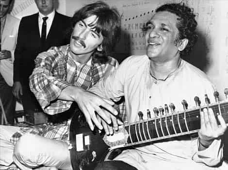 George Harrison, of the Beatles, left, sits cross-legged with his musical mentor, Ravi Shankar, in Los Angeles, as Harrison explains to newsmen that Shankar is teaching him to play the sitar.