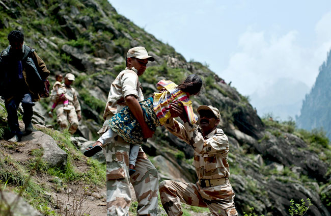 Indo-Tibetan Border Police personnel carry a child as they provide rescue assistance for stranded pilgrims after a section of road was washed away in Govind Ghat. AFP Indo-Tibetan Border Police personnel carry a child as they provide rescue assistance for stranded pilgrims after a section of road was washed away in Govind Ghat. AFP