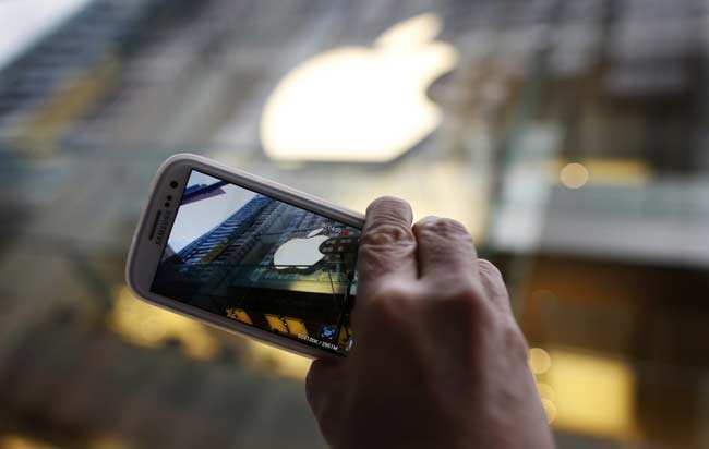 A passerby photographs an Apple store logo with his Samsung Galaxy phone on the morning iPhone 5 goes on sale to the public in central Sydney in this September 21, 2012 file photograph. Reuters/Tim Wimborne/Files