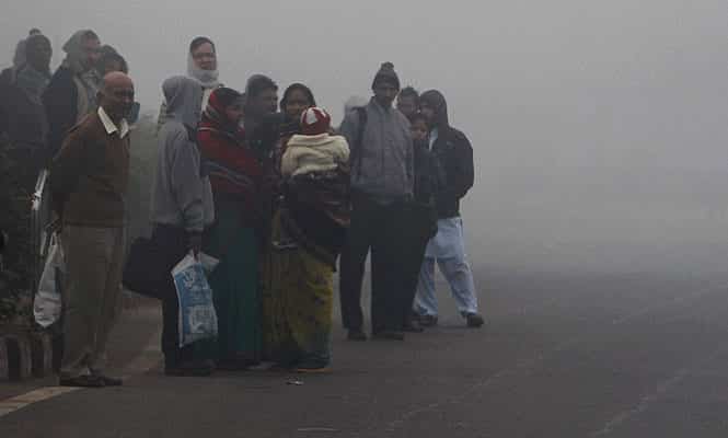 Commuters, wrapped in woollens, wait for bus at a bus stop on a foggy morning in New Delhi. (PTI)</font></em></strong)