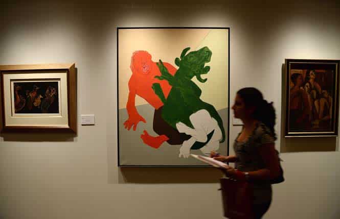 A visitor walks past Rabindra Nath Tagore's "Untitled", Tyeb Mehta's "Mahisasura" and Ram Kumar's "Family", during a media preview ahead of Christie's first auction in Mumbai. (AFP)</font></em></strong)
