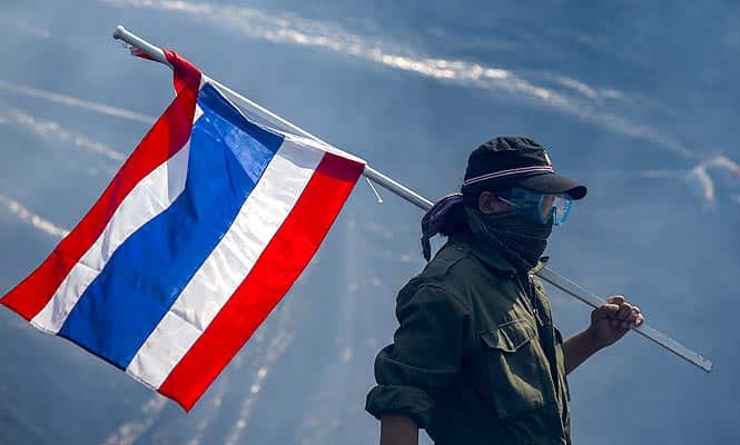 An anti-government protester carries a Thai national flag as he walk away from teargas during clashes with the police the metropolitan police headquarters in Bangkok. (Reuters photo)</em)