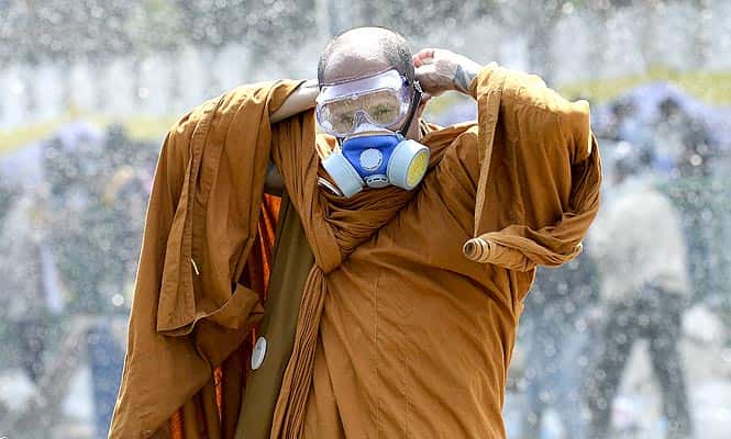A monk puts on a gas mask as riot police use water cannon and tear gas while anti-government protesters attempt to remove barricades outside government house in Bangkok. (Reuters photo)</em)