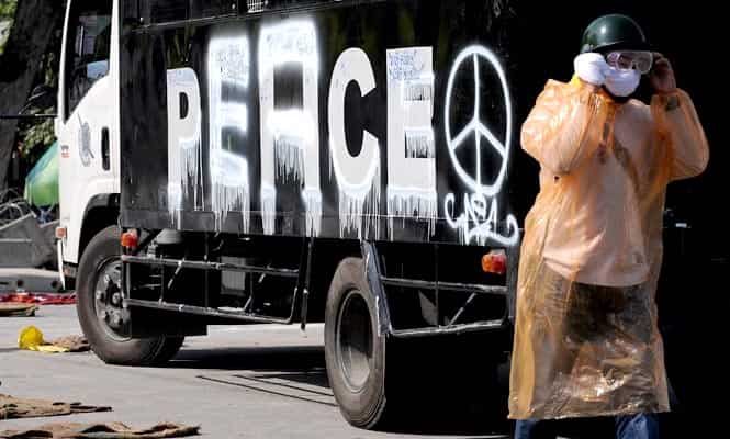 An anti-government protester walks past a police vehicle with the word 'police' painted into 'peace' outside the government house in Bangkok. (AFP photo)</em)