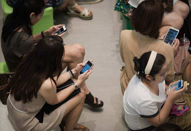 A group of people sitting down using their smartphones at a shopping mall in Bangkok. Photo: AFP / Nicolas Asfouri A group of people sitting down using their smartphones at a shopping mall in Bangkok. Photo: AFP / Nicolas Asfouri