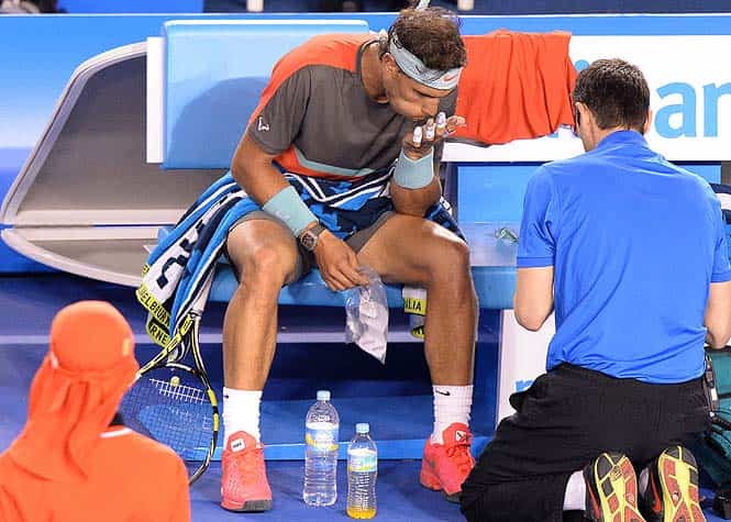 Spain's Rafael Nadal (C) blows on his injured hand as he receives treatment during his men's singles semi-final match against Switzerland's Roger Federer on day twelve of the 2014 Australian Open. (AFP Photo)