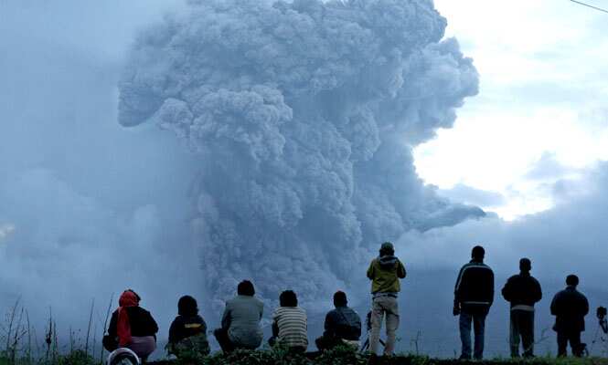 Indonesian men watch Mount Sinabung spewing volcanic materials during an eruption in Tiga Kicat, North Sumatra, Indonesia. (AP Photo) 
</div)