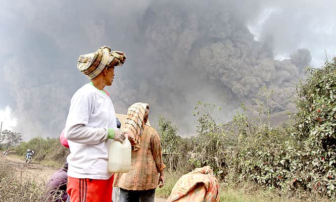 Villagers watch as Mount Sinabung releases pyroclastic flows during an eruption in Namantaran, North Sumatra, Indonesia. (AP Photo) 
</div)