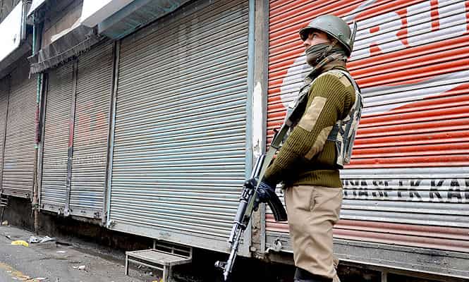 A paramilitary trooper stands guard in front of shuttered shops during a curfew in Srinagar. (AFP Photo)
</div) A paramilitary trooper stands guard in front of shuttered shops during a curfew in Srinagar. (AFP Photo)
</div)