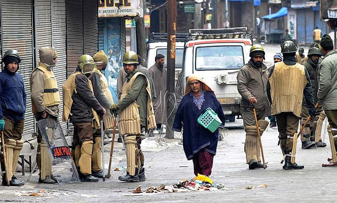 A Kashmiri woman walks past police personal standing near a barbed wire roadblock during a curfew in Srinagar. (AFP Photo)
</div) A Kashmiri woman walks past police personal standing near a barbed wire roadblock during a curfew in Srinagar. (AFP Photo)
</div)
