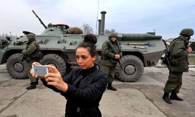 A woman takes photos in front of armed servicemen and their armoured personnel carrier in the eastern Crimea's port city of Feodosiya. A woman takes photos in front of armed servicemen and their armoured personnel carrier in the eastern Crimea's port city of Feodosiya.