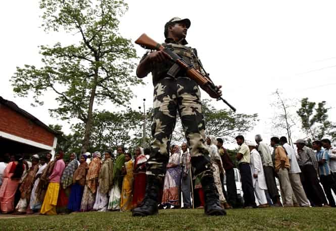 A security personnel stands guard as people line up to cast their vote outside a polling station in Nakhrai village in Tinsukia district in, Assam. (Reuters Photo)</em) A security personnel stands guard as people line up to cast their vote outside a polling station in Nakhrai village in Tinsukia district in, Assam. (Reuters Photo)</em)