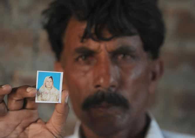 Mohammad Iqbal poses for a photograph as he holds up an image of his wife Farzana. (AFP Photo)</em> 
</div)