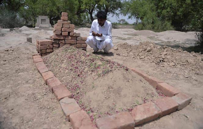 Mohammad Iqbal prays at the grave of his wife Farzana. (AFP Photo)</em> 
</div)