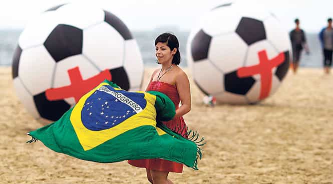 A woman with a Brazilian flag walks in front of giant soccer balls with red crosses, as part of a protest against government outlays for the FIFA World Cup. (Photo: EPA)</font></em) A woman with a Brazilian flag walks in front of giant soccer balls with red crosses, as part of a protest against government outlays for the FIFA World Cup. (Photo: EPA)</font></em)
