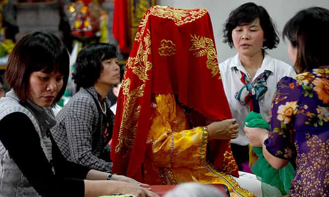 A "Len Dong" dancer (C) is being dressed up before she performs a new dance at a local temple in Hanoi. (AFP Photo)</em)