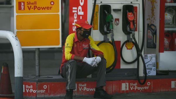 A petrol station worker wearing a facemask waits for customers while sitting next to a petrol pump.