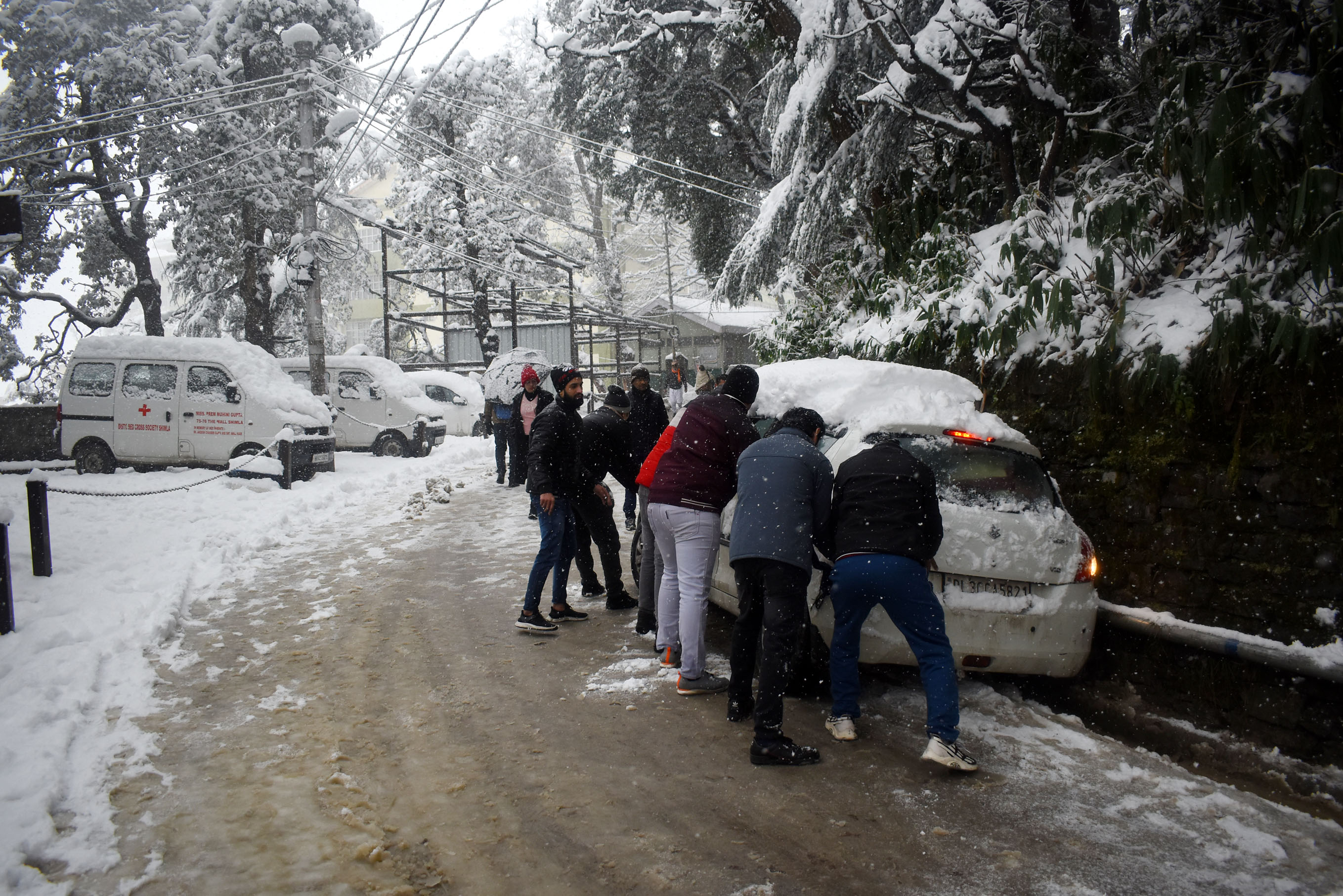 People try to push a vehicle stuck on the snow covered road during heavy snowfall at Sanjauli-IGMC Hospital road near Sanjauli in Shimla. People try to push a vehicle stuck on the snow covered road during heavy snowfall at Sanjauli-IGMC Hospital road near Sanjauli in Shimla.