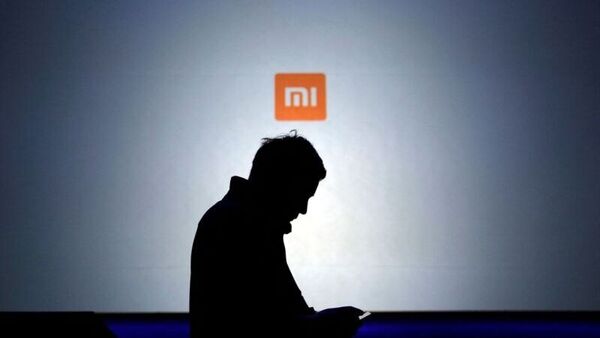 File photo - A man uses his mobile phone in front of a screen showing a logo of Xiaomi. (REUTERS)