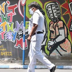 মাস্ক করে একটি গ্র্যাফিটি আঁকা দেওয়ালের পাশ দিয়ে হেঁটে যাচ্ছে এক পুলিশকর্মী (ছবি সৌজন্য পিটিআই)