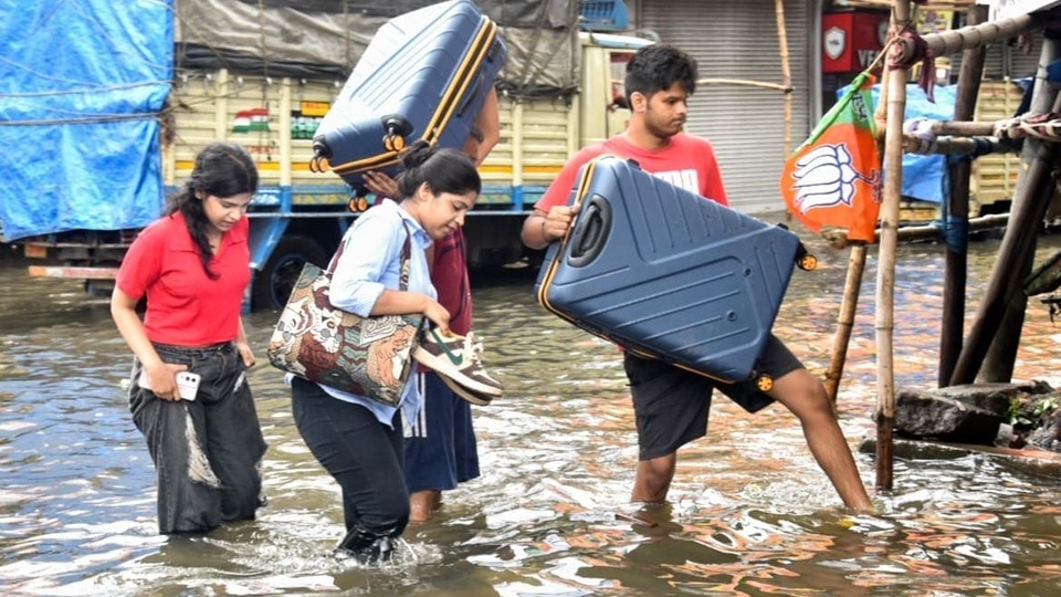রাতভর ভারী বৃষ্টির পর জলাবদ্ধ রাস্তায় তাদের জিনিসপত্র নিয়ে জলে হেঁটে যাচ্ছেন যাত্রীরা।(Saikat Paul/ANI)