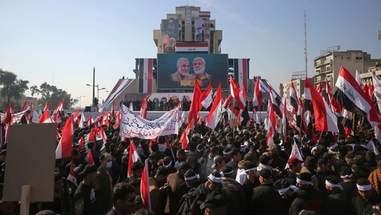 Iraqi demonstrators lift flags and placards as they rally in Tahrir square in the capital Baghdad on January 3, to mark one year after a US drone strike killed Iran's revered commander Qasem Soleimani (billboard L) and his Iraqi lieutenant Abu Mahdi al-Muhandis (billboard R) near the capital.(Ahmad Al-Rubaye / AFP)