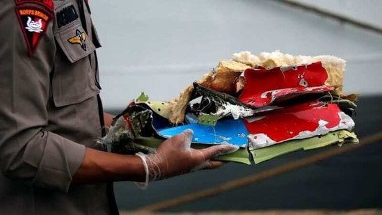 An Indonesian police officer carries debris of Sriwijaya Air flight SJ 182, at Tanjung Priok port in Jakarta on January 10. Pieces of wreckage were brought to Jakarta port by rescuers. One twisted piece of metal was painted in Sriwijaya Air's blue and red colours. Indonesian authorities said they had also retrieved body parts and clothing, Reuters reported.(WIlly Kurniawan / REUTERS)