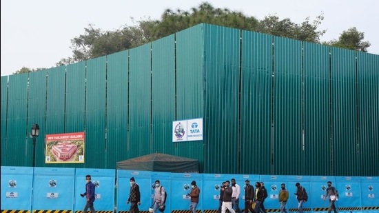 Pedestrians wearing walk past the construction site for the new Parliament building, part of the Central Vista redevelopment project, in New Delhi. (Bloomberg) Pedestrians wearing walk past the construction site for the new Parliament building, part of the Central Vista redevelopment project, in New Delhi. (Bloomberg)
