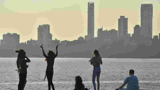 Young people enjoy the clear weather while a senior citizen practises yoga on the promenade at Marine Drive. (HT PHOTO).