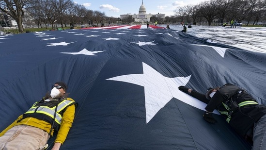 Workers use their body weight to hold down a large American flag placed on the National Mall, with the US Capitol behind them, on January 18 in Washington.(Alex Brandon / AP)