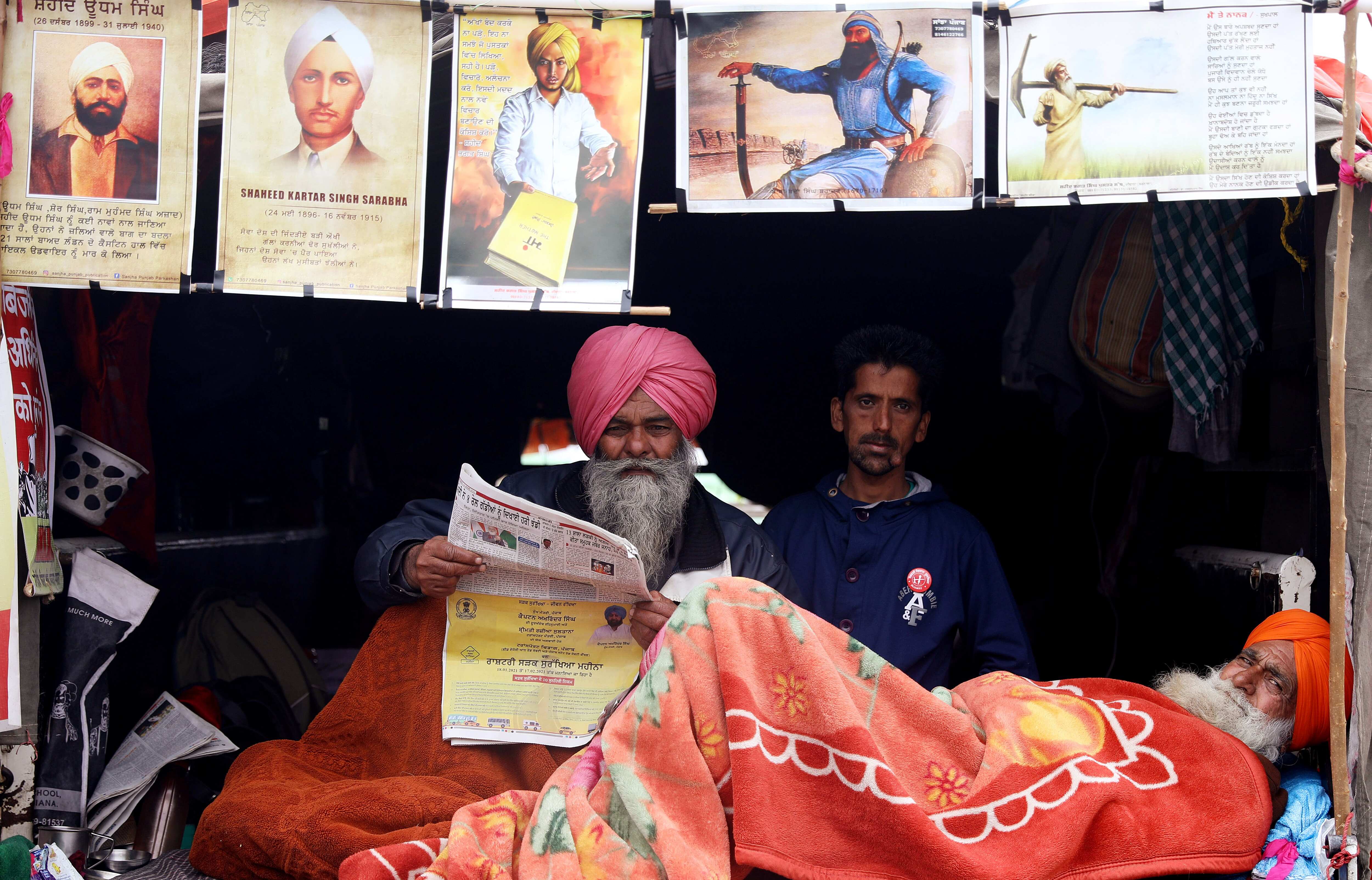 A farmer reads a Newspaper under a tent covering with posters during a protest against new farm laws at Singhu Border, in New Delhi. (ANI) A farmer reads a Newspaper under a tent covering with posters during a protest against new farm laws at Singhu Border, in New Delhi. (ANI)