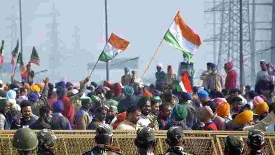 Farmers hold flags as police personnel stand guard behind barricades during protests against new farm laws at Ghazipur (Delhi-UP border). (Sakib Ali / HT Photo) Farmers hold flags as police personnel stand guard behind barricades during protests against new farm laws at Ghazipur (Delhi-UP border). (Sakib Ali / HT Photo)