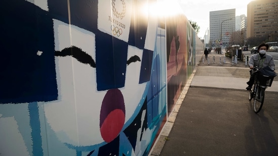 A man wearing a mask rides past Tokyo's Olympics mascot shown on the wall of a construction site in Tokyo on Friday, Jan. 22, 2021.(AP) A man wearing a mask rides past Tokyo's Olympics mascot shown on the wall of a construction site in Tokyo on Friday, Jan. 22, 2021.(AP)