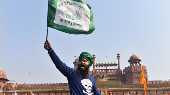 A farmer waves a flag as more farmers gather at Red Fort during their tractor parade on Republic Day, in New Delhi. (PTI)