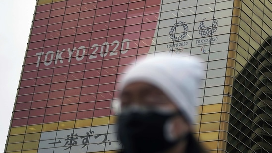A man wearing a protective mask to help curb the spread of the coronavirus walks near a banner of the Tokyo 2020 Olympics and Paralympics.(AP) A man wearing a protective mask to help curb the spread of the coronavirus walks near a banner of the Tokyo 2020 Olympics and Paralympics.(AP)