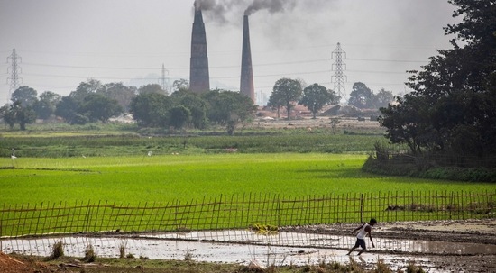 A farmer works in his paddy field as smoke rises from brick kilns on the outskirts of Guwahati(AP Photo)