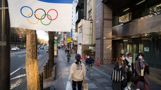 People wearing face masks walk and ride past an Olympics decoration installed along a street in Tokyo.(AP) People wearing face masks walk and ride past an Olympics decoration installed along a street in Tokyo.(AP)