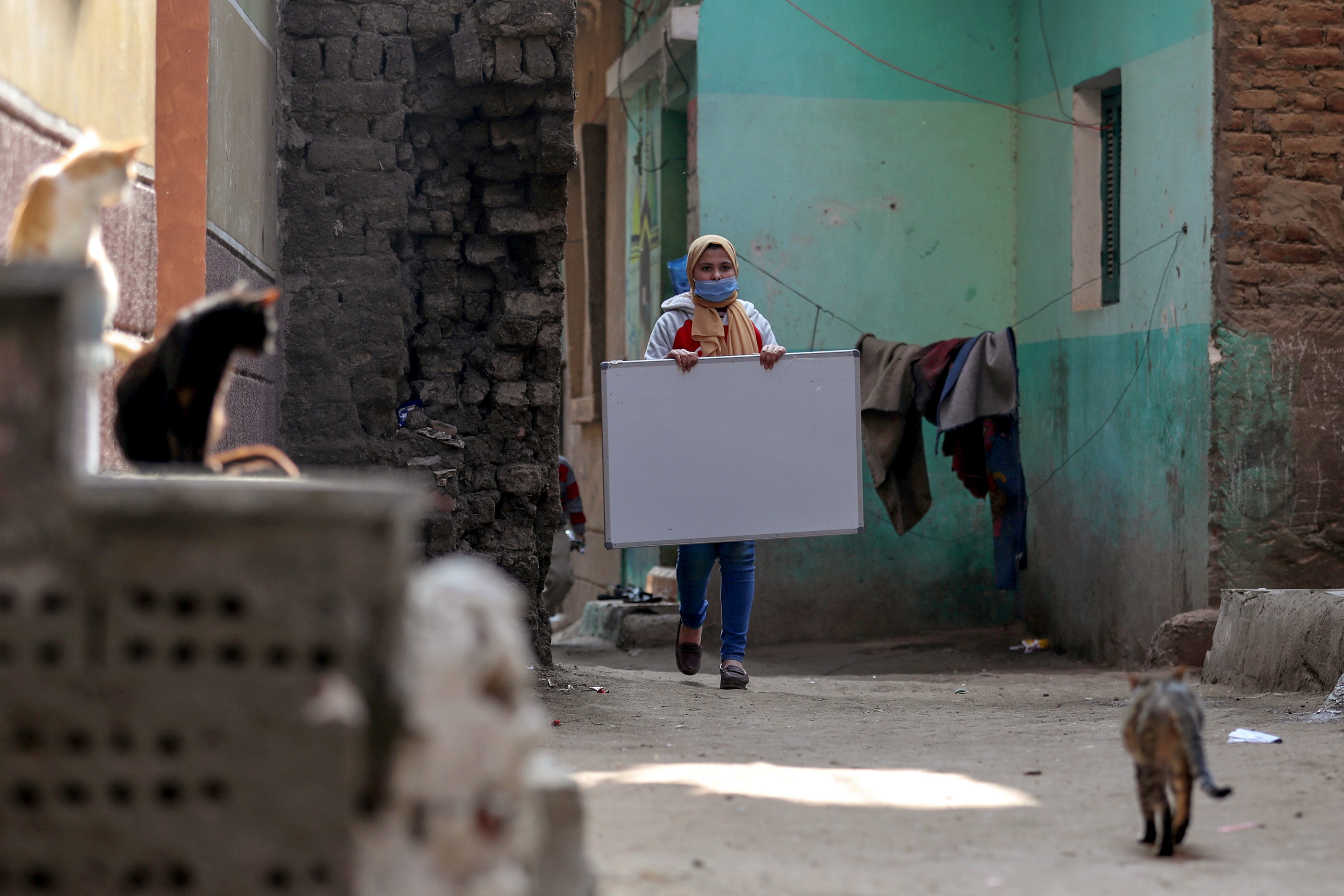 Reem El-Khouly, a 12-year-old girl, holds a board as she makes her way to teach children in her neighborhood. (REUTERS)