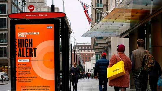 Pedestrians walk past Tier 2 Coronavirus information displayed on an electronic advertising board at a bus stop in central London on December 14, 2020. - The majority of England's 55 million population are under Tier 2 or 3 restrictions, depending on local infection rates. London -- Britain's capital and driving force of the UK economy -- is currently in Tier 2, meaning pubs where food is served and restaurants can open, obeying social distancing rules. But in Tier 3 areas, hospitality venues have to close except for takeaways. (Photo by Tolga Akmen / AFP)(AFP)