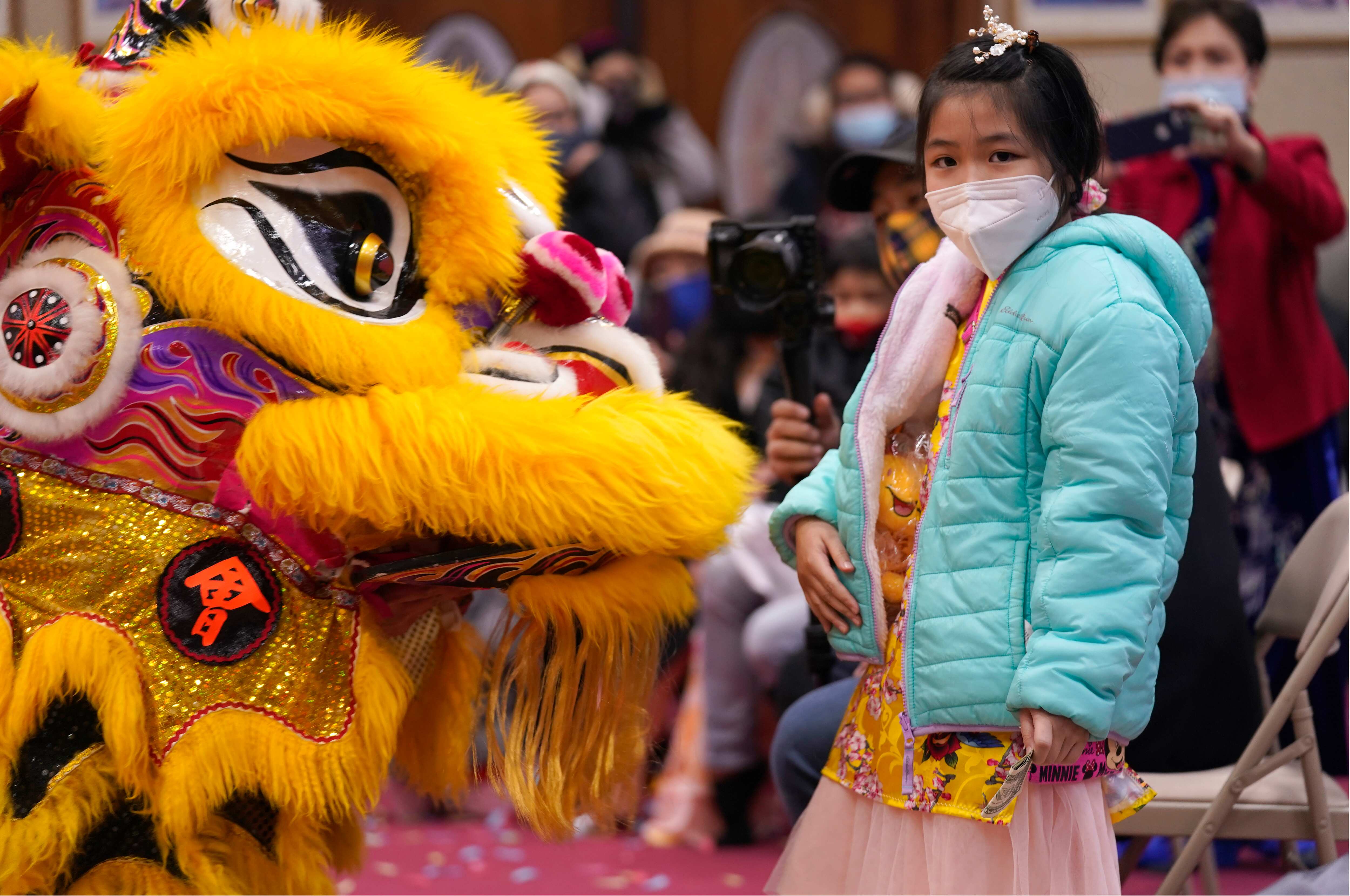 Wearing a mask to prevent the spread of COVID-19, Anna Lee, 9, stands next to lion dancers. (AP)
