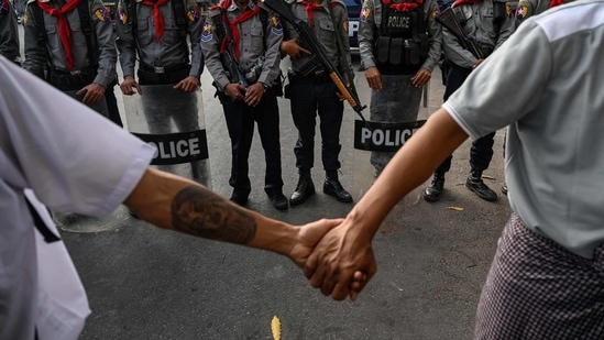 Demonstrators hold hands as armed police personnel stand guard during the ongoing protest against Myanmar’s military coup, at National League for Democracy (NLD) headquarters in Yangon on February 15. Peaceful demonstrations against the military takeover resumed on February 16, following internet shutdown for a second straight night and violence against protesters a day earlier by security forces.(Ye Aung Thu / AFP)
