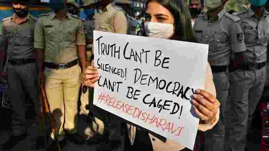 A woman holds a placard next to policemen during a protest against the arrest of climate activist Disha Ravi, in Bengaluru, India.(Reuters)