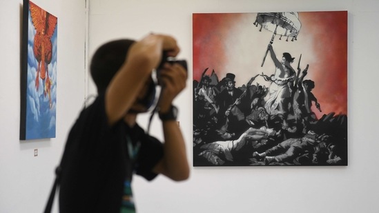 A man takes a photograph of paintings by graffiti artist "Headache Stencil" at the "112 the Exhibition" event at WTF Gallery and Cafe in Bangkok, Thailand, February 13, 2021. (REUTERS)