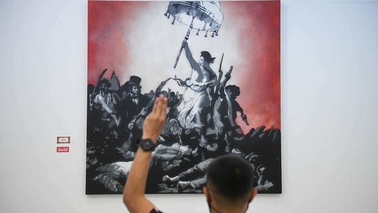 A man flashes a three-finger salute as he stands in front of a painting by graffiti artist "Headache Stencil" in the "112 the Exhibition" at WTF Gallery and Cafe in Bangkok, Thailand, February 13, 2021.(REUTERS)