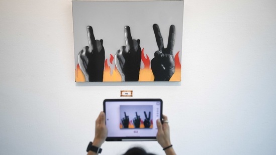 A man takes a photograph of a painting by graffiti artist "Headache Stencil" during the "112 the Exhibition" at WTF Gallery and Cafe in Bangkok, Thailand, February 13, 2021.  (REUTERS)