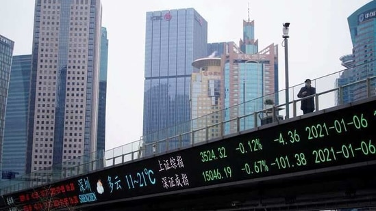 A man stands on an overpass with an electronic board showing Shanghai and Shenzhen stock indexes, at the Lujiazui financial district in Shanghai, China.(REUTERS)