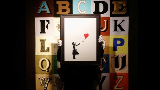 An art handler poses with "Girl With a Balloon" by Banksy, in front of "Alphabet" by Sir Peter Blake, as preparations take place at Bonhams auction house ahead of their British Cool art sale, in London, Britain, February 22, 2021. REUTERS/John Sibley NO RESALES. NO ARCHIVES. TPX IMAGES OF THE DAY(REUTERS)