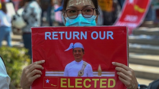 An anti-coup protester with thanaka, a traditional face paste with letters CDM, representing "Civil Disobedience Movement," displays a placard with an image of deposed Myanmar President Win Myint during a street march in Mandalay on February 25.(AP)