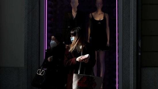 Women wearing a face mask walk past a fashion store's front window in Monte Napoleone shopping street during the Fashion Week, in Milan, Italy, Wednesday, Feb. 24, 2021. (AP)