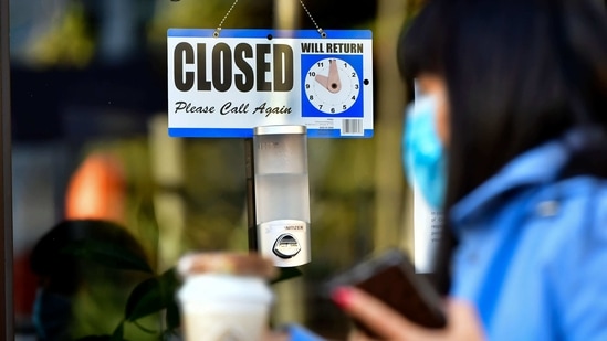 A pedestrian wearing her facemask and holding a cup of coffee walks past a closed sign hanging on the door of a small business in Los Angeles, California.(AFP) A pedestrian wearing her facemask and holding a cup of coffee walks past a closed sign hanging on the door of a small business in Los Angeles, California.(AFP)